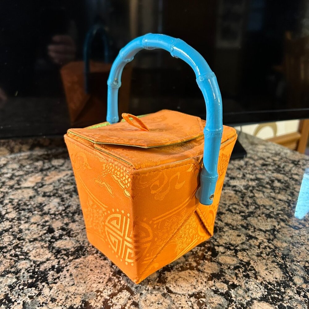 Ladies orange purse with a blue handle shaped like a Chinese carry-out container